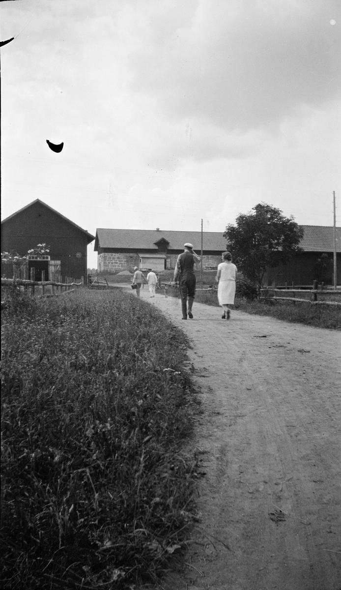 Personer på väg mot ekonomibyggnader vid Revelsta gård, Altuna socken, Uppland 1927