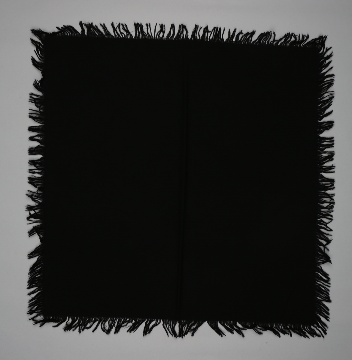 Firkanta (kvadratisk) sjal i svart ullstoff. Frynsar på alle sidane.