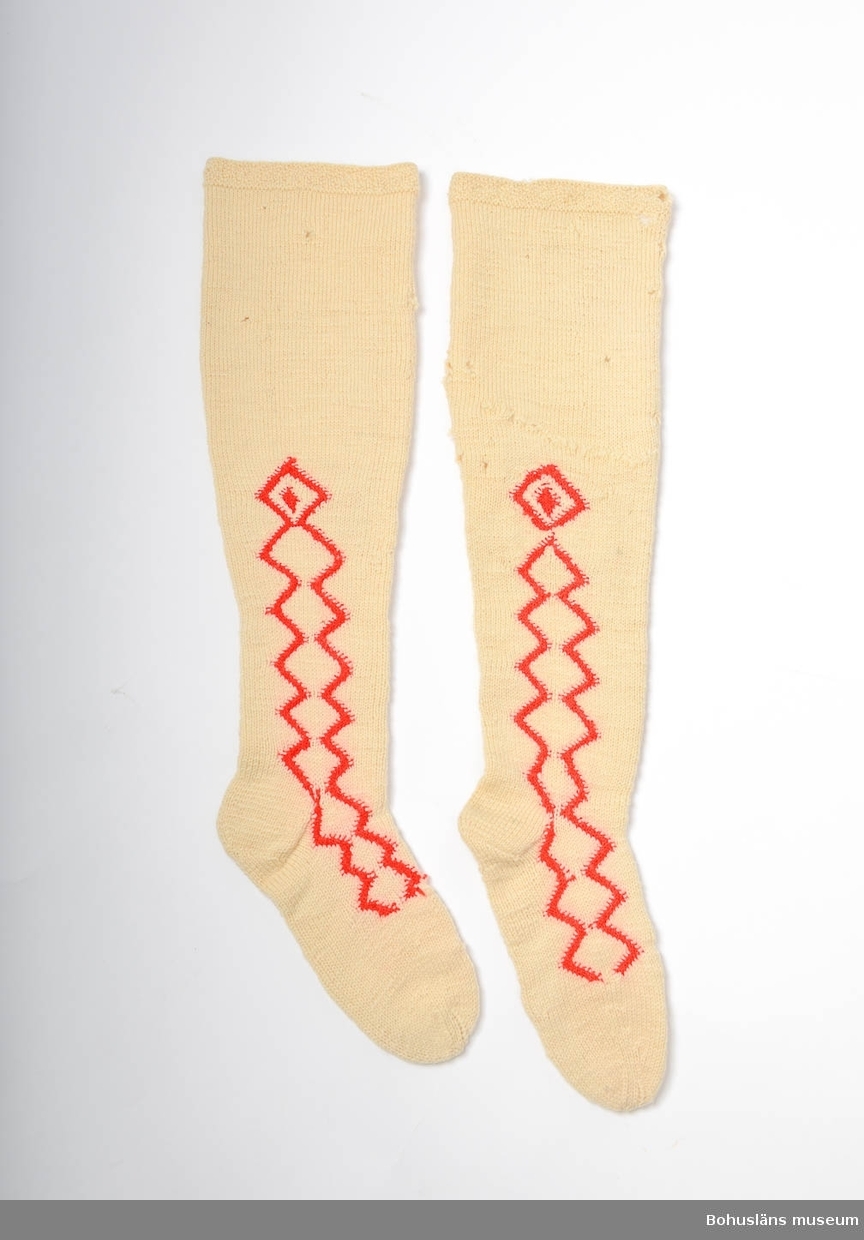 Handstickade strumpor av vitt ullgarn, slätstickade med sicksack-mönster i aviga maskor med rött ullgarn längs fötterna och halvvägs upp på skaften, på både in och utsida. Överst har strumporna en kant mönstrad med aviga och räta maskor. Märkta UM 4:B:I och II.
Enligt Knut Adrian Anderssons katalog I:5:4, D 2 A:1 i museets arkiv, är strumporna "stickade ur minnet av en gammal kvinna på Inland i början av 1900 talet". I samma katalog står även att de vita strumporna skänkta 1910 av Bertha Kleberg är stickade av "gummor på Inland".
Små hål på många ställen. Flera lagningar bl a en lagad lång reva på ena skaftet.
Strumporna diskuteras och är avbildade i Centergran (2010) s. 27-28.

Litteratur om Bertha Kleberg och om revitalisering av bygdedräkter:
Arill, David, Bertha Kleberg och Bohusdräkten ur Bohusländska folkminnen Studier och uppteckningar red Arill, David, Uddevalla 1922.
Centergran, Ulla, Folkdräktsrörelsen i Bohuslän och Göteborg, C-uppsats i etnologi, Göteborg 1973, Bygdedräkter bruk och brukare, Göteborg 1996. 
Centergran, Ulla. Bohusdräkter. Tolkningar under ett sekel. Bohusläns museum och Bohusläns hembygdsförbund, nr. 71. Bohusläns museums förlag. Andra upplagan 2010. 
Wistrand P G, Bohusländska folkdräkter ur Fataburen häfte 1 1908.
STÖDTYG FASTTRÅCKLAT INUTI SKAFTEN PÅ BÅDA STRUMPORNA
Omkatalogiserat 1997-03-20 VBT

Enligt uppgifter på diarienummer 184/69 KVINNLIGA DRÄKTPLAGG FRÅN BOHUSLÄN TILL UDDEVALLA MUSEUM: Strumporna 4a, 4b, 4c är stickade av gummor på "Inland" i början av 1900-talet. ...

Ur handskrivna katalogen 1957-1958:
Strumpor 3 par.
a) Ett par  a) 1-2 L. c:a 62 cm; röda, ylle, stickade m. resår i skaftets översta del; malhål. 
b) ett par b:1-2; L. c:a 67 cm, ylle, vita m. instickade röda kilar; malhål. 
c) Ett par c: 1-2; L. c:a 55; vita, bomull, m. instickade  röda kilar, några rostfläckar. 

Lappkatalog: 78