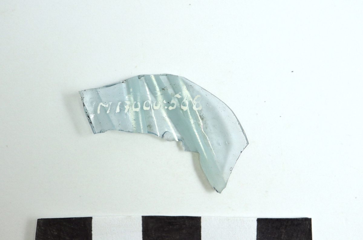 Ett ornerat venetianskt glas i svagt blå färg. På glaset finns två skikt pålagda vita trådar, (vetro a fili) i relief. Ser ut som M 17000:565 - 567 och tillhörande samma eller liknande kärl.