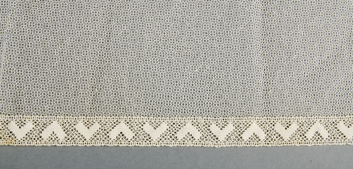 Schal av vitt tyll, dubbelt tyg med tyllspets i ena kanten.
Har använts på huvudet.