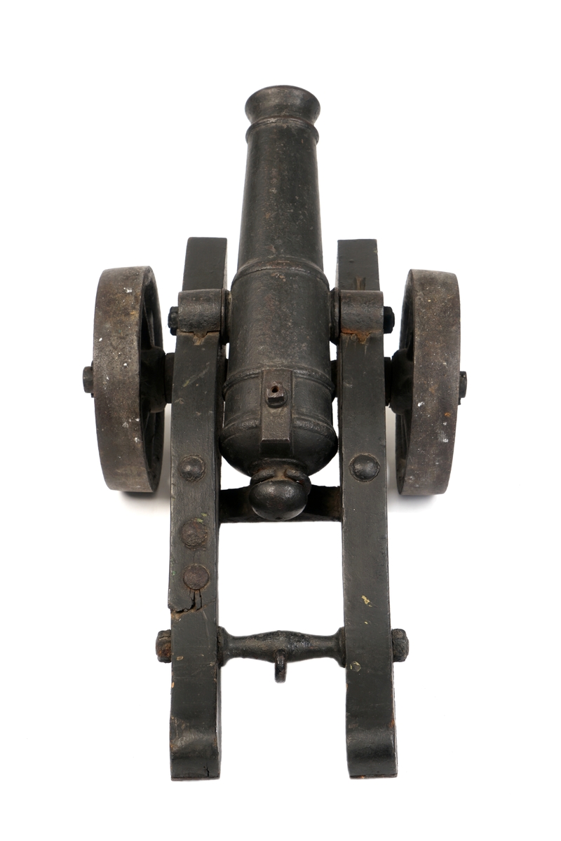 Kanon av jern.Sortmalt.På sortmalt understell/lavett av tre med jernbeslag og hjul av jern.