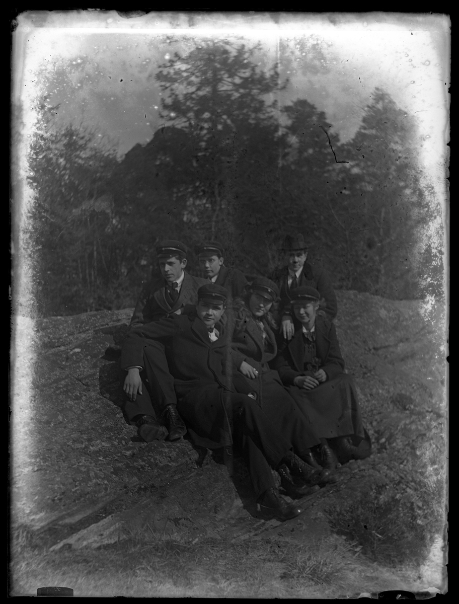 Gruppbild med Gustav K (troligen Kronberg), Greta B., Halvar, Einar (troligen Olsson), Vera & Mia K sittandes på en sten med träd i bakgrunden.