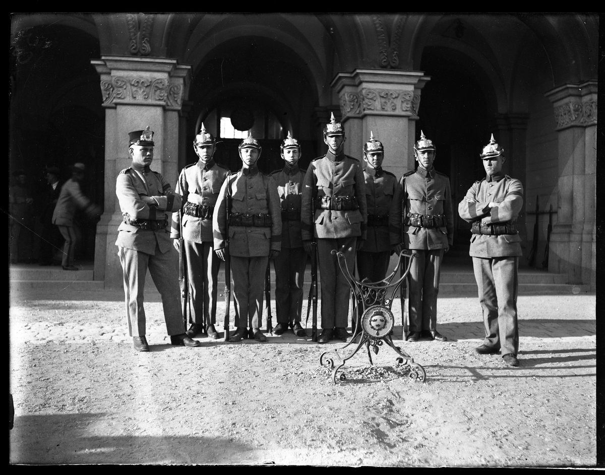 Gruppbild på livkompaniets (I1) kasernvakt i grå uniformer, hjälmar och vapen.