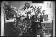 Fru Dahlgren sitter i en korgstol i ett finrum omgiven av blommor. Porträttet taget i samband med 60årsdagen.