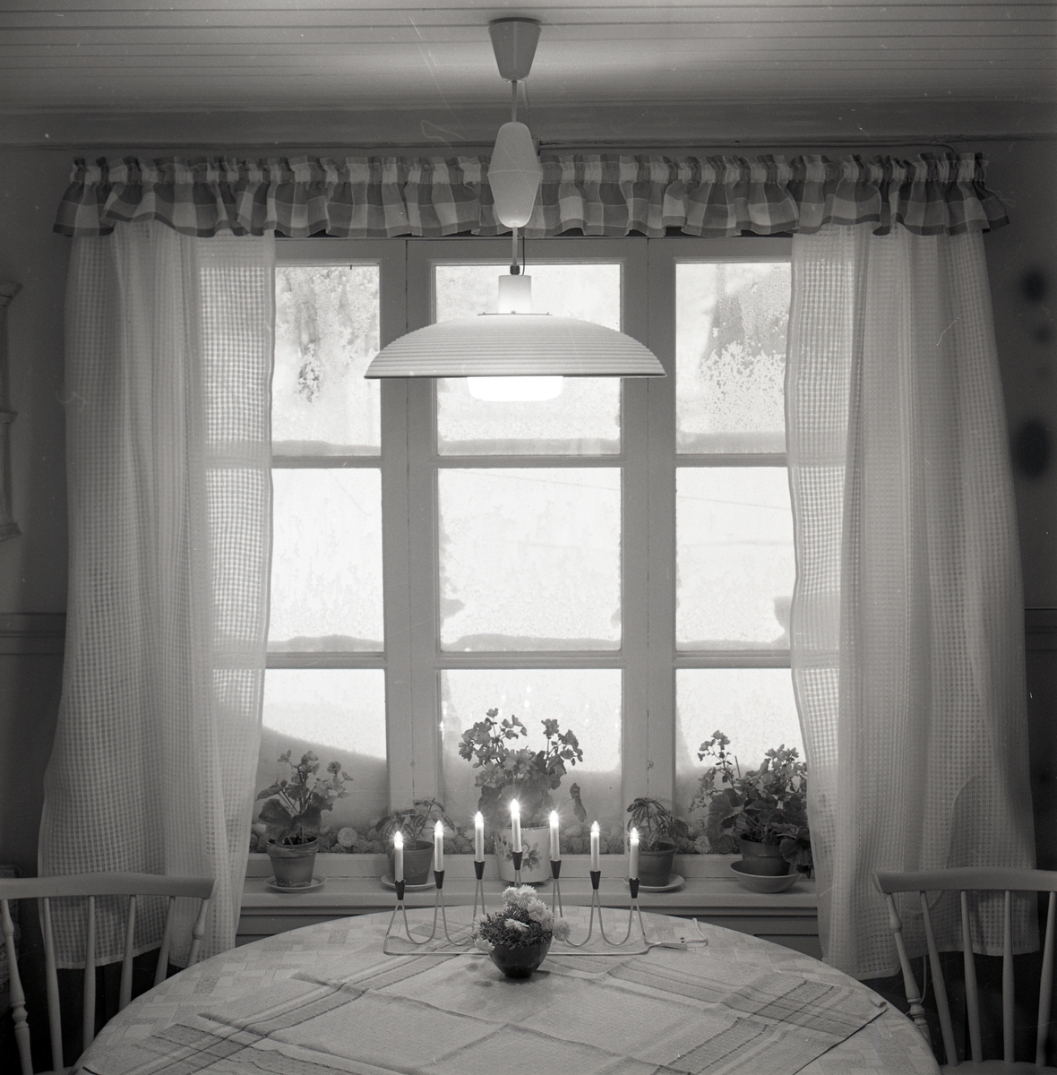 Ett fönster med gardiner bakom ett bord dekorerat med en adventsljusstake i december 1968.