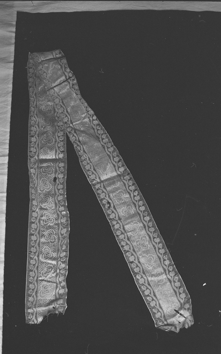 Bredt silkebånd med damaskmønster i midten og mønster op gjennomsiktig bunn i kanene.