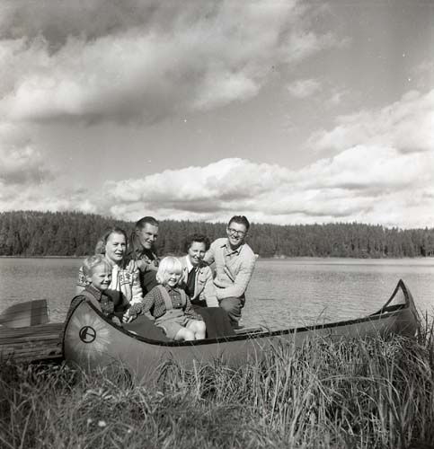 En grupp med bland andra Hilding Mickelsson poserar intill en kanot. Bakom gruppen syns skidtjärn, 1950.