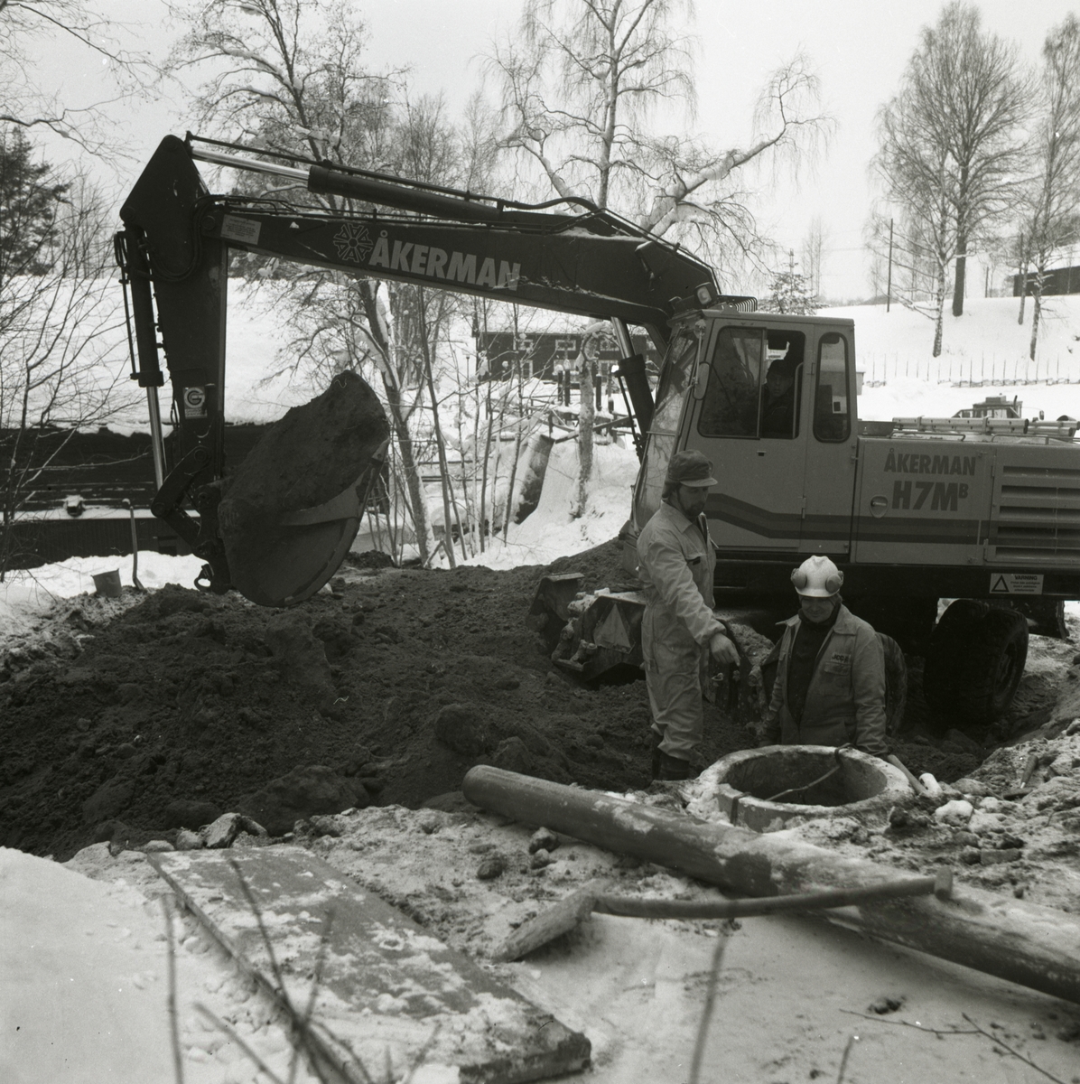 Två män vid en grävmaskin i snöigt landskap.