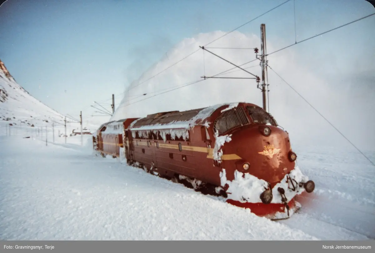 Snørydding ved Oksebotn km 295, mellom Finse og Haugastøl, etter at nattoget fra Bergen til Oslo, tog 606, hadde kjørt seg fast. Diesellokomotiv type Di 3 nr. 602 og roterende snøplog DiR1 nr. 501.