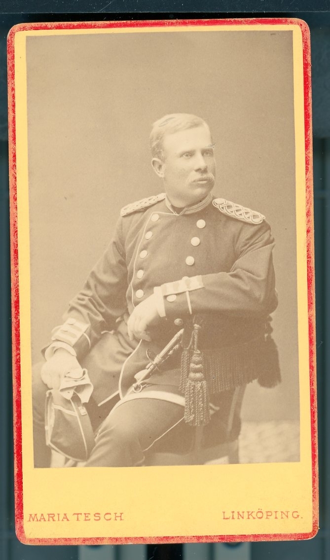 Kabinettsfotografi: Johannes Petrelli i uniform med mössa och handskar i handen sittande bakåtvänd i en stol.