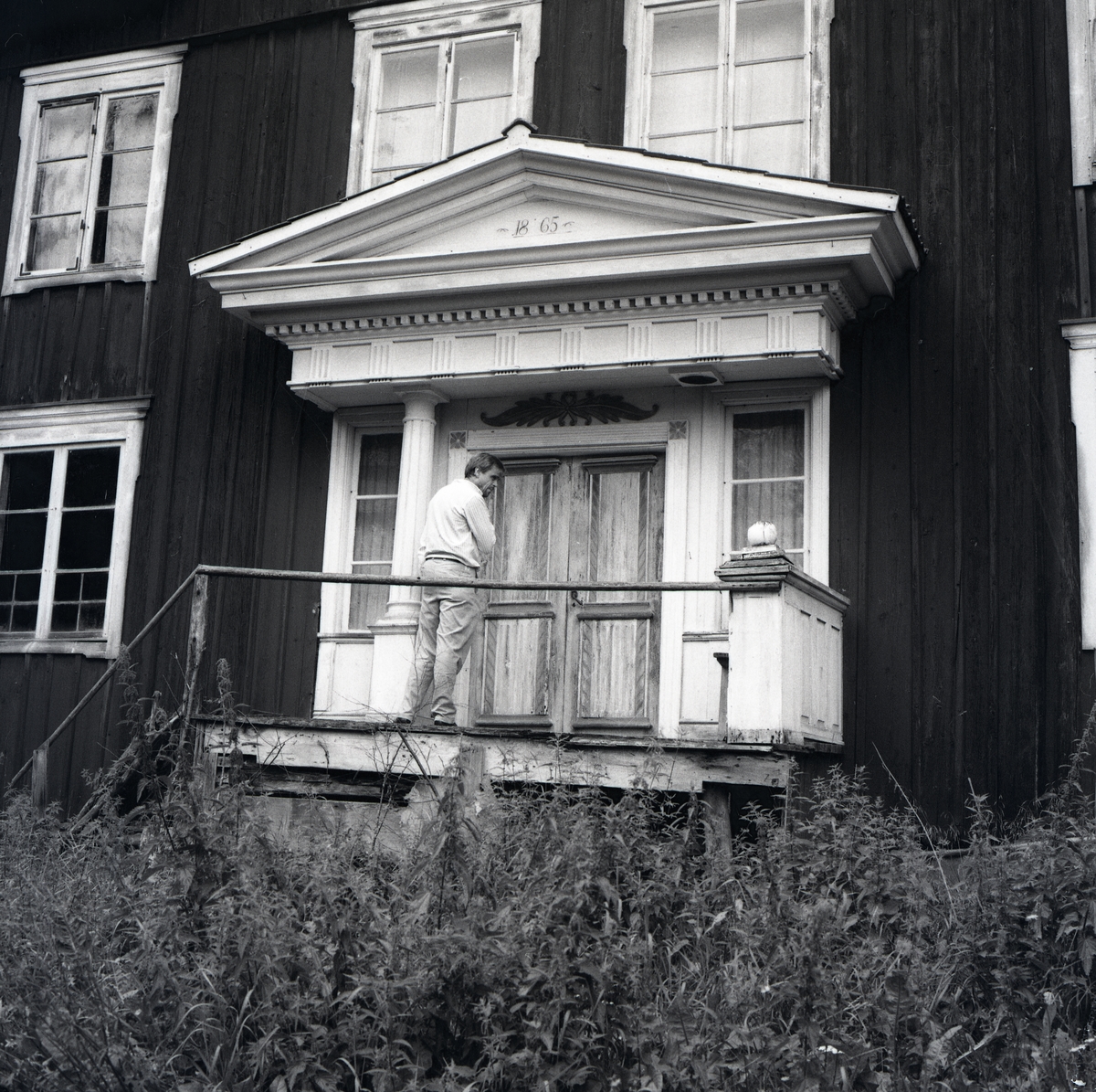 En man står på en ranglig brokvist framför ett hus i Grängsbo.
