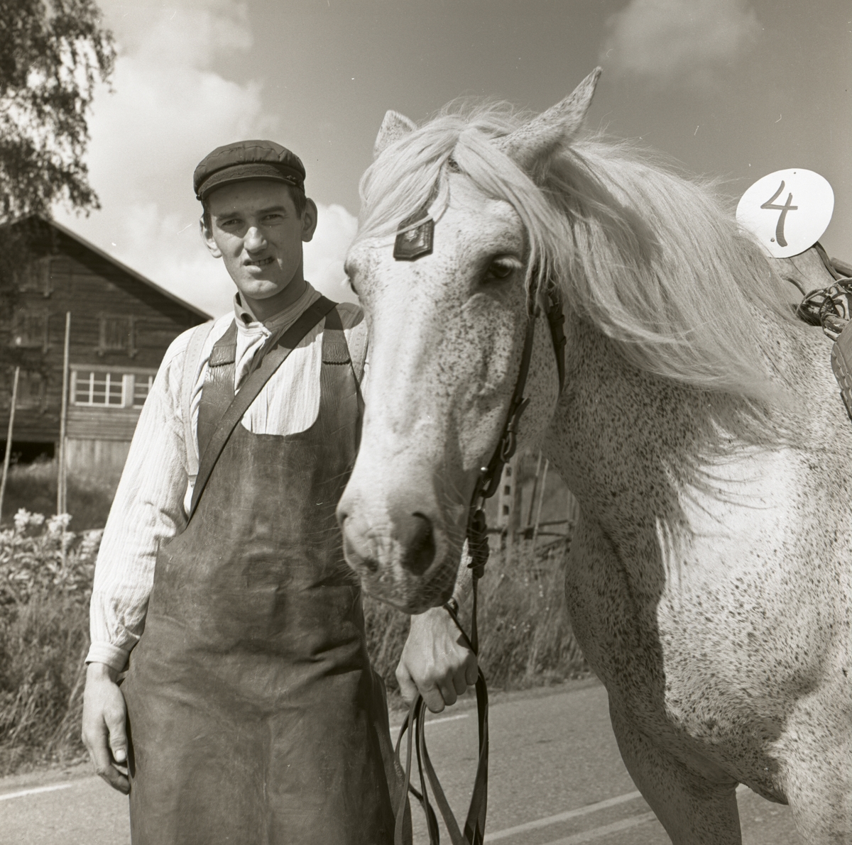 En deltagare i Hembygdsfestens karneval i Rengsjö. Han är iklädd keps och skinnförkläde samt står bredvid en häst, 22 juli 1962.
