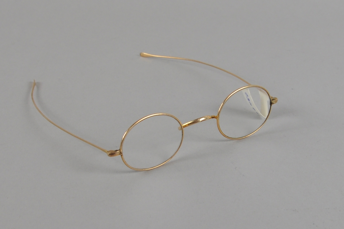 Ovale briller med gullfarget metallinnfatning. Lange brillestenger.