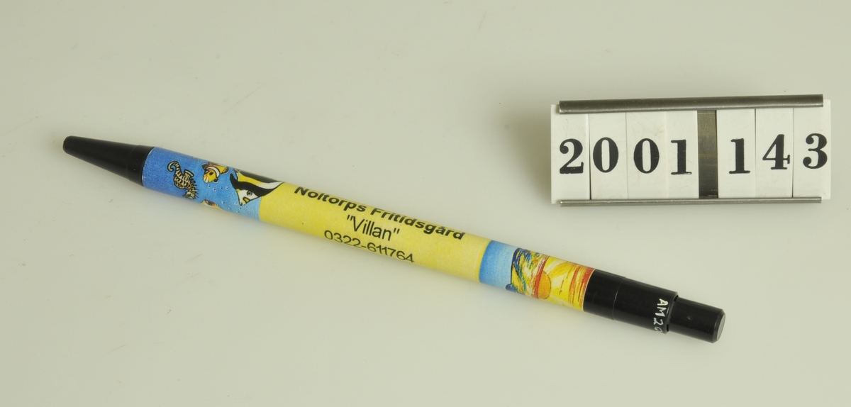 
Pennan har svarta ändar, mitten är gul med solnedgångs- och fiskmotiv. Försedd med texten:: Noltorps fritidsgård "Villan" 0322-61 17 64  ALINGSÅS. Tillvaratagen av museets personal.