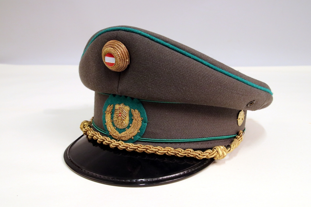 Grå uniformslue med sort lakkskjerm og detaljer i gull og grønt.