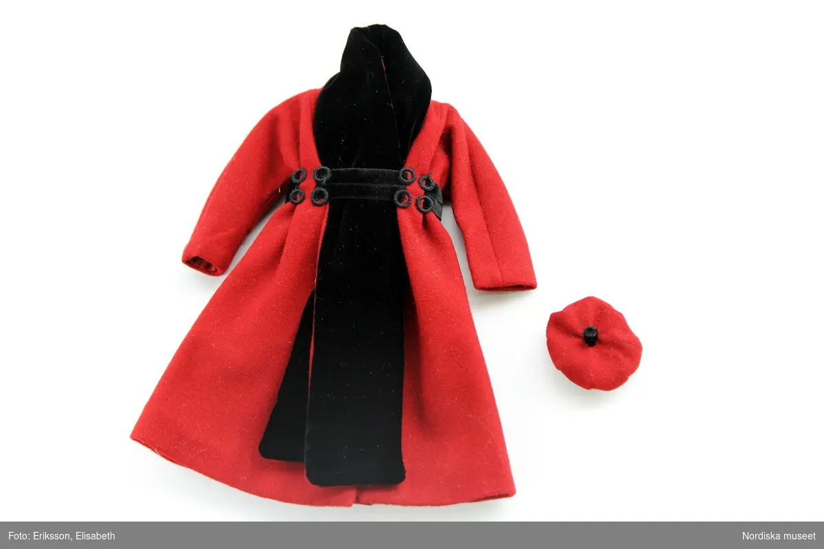 Katalogkort:

a) Kappa, röd med svart garnering, hatt.