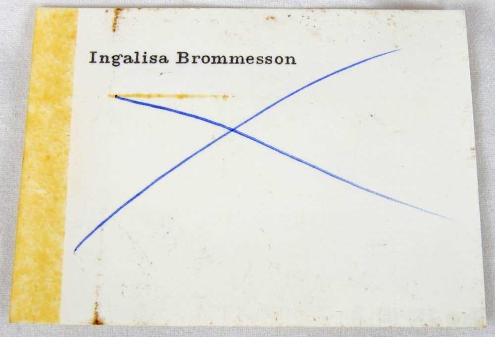 Rektangulär kliché (1) av brunmålad metall. Högst upp i höger hörn finns texten: "Ingalisa Brommesson", präglad. 

Till finns ett vitt, rektangulärt visitkort (2) av papper. Högst upp i vänster hörn finns texten: "Ingalisa Brommesson", tryckt i svart. På mitten finns ett kryss ritat med blått bläck.