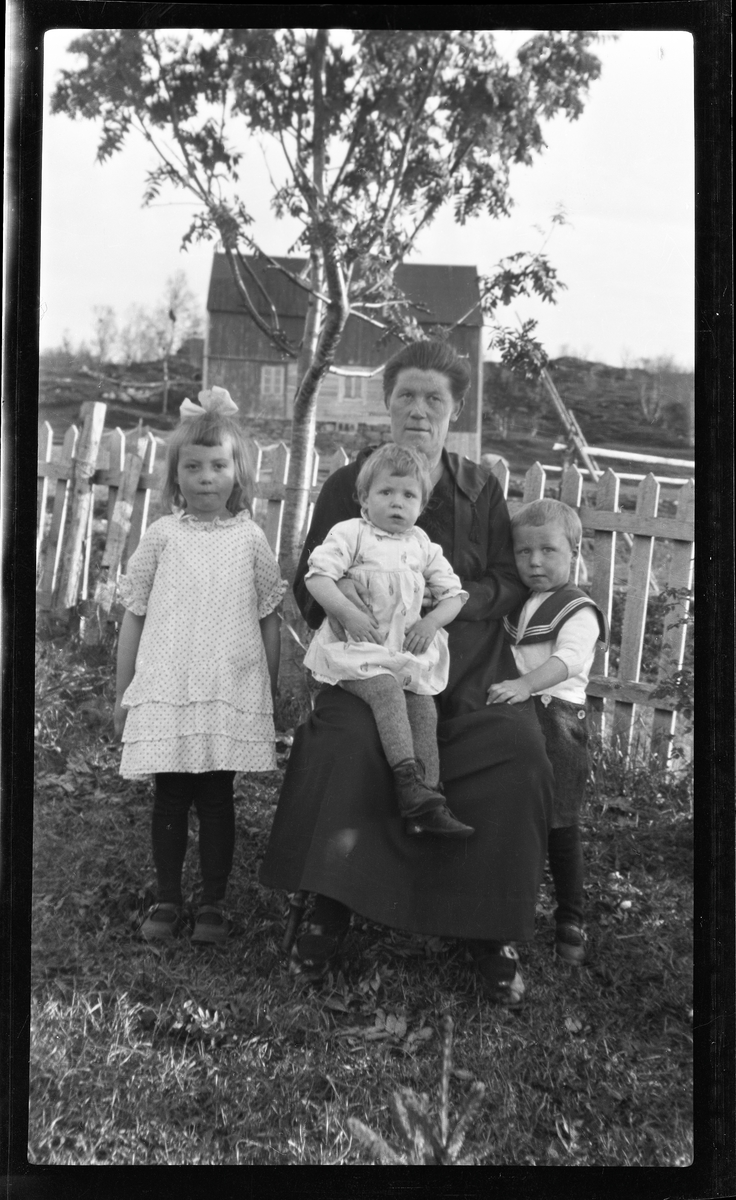 Gruppeportrett av en kvinne og tre barn i hage.