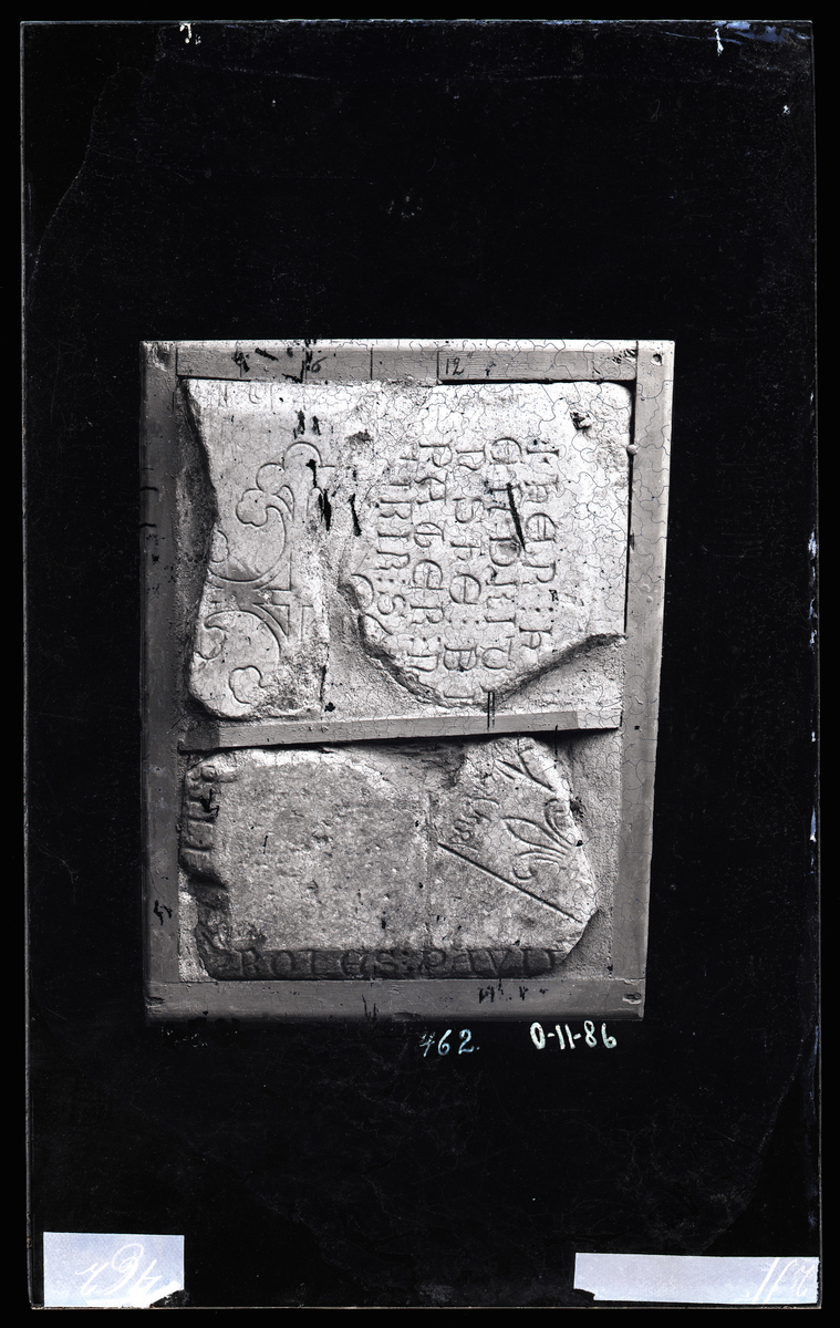 Deler av to gravsteiner fra middelalder (ca. 1300-tallet) fra Nidarosdomen. 

Øverste stein er dekorert med et liljekors. 

Nederste stein har en lilje og delvis tekst på latin: ... BILI : PROLES : PAVLV

"Nobilium proles Paulus" - Pål av adel ætt