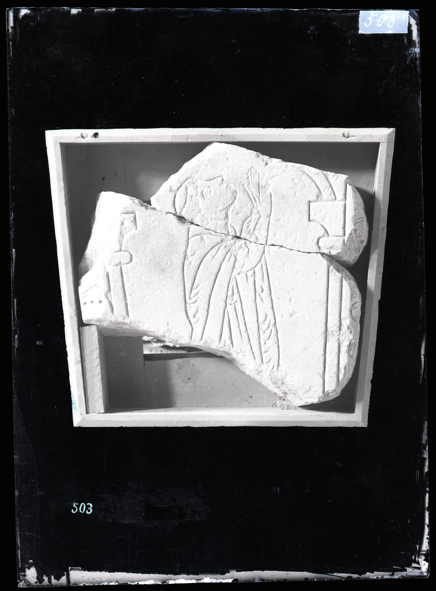 Prestegravstein fra middelalder (1300-tallet) fra Nidarosdomen. Den avdøde løfter hendene til bønn, og er kledd i kjortel.