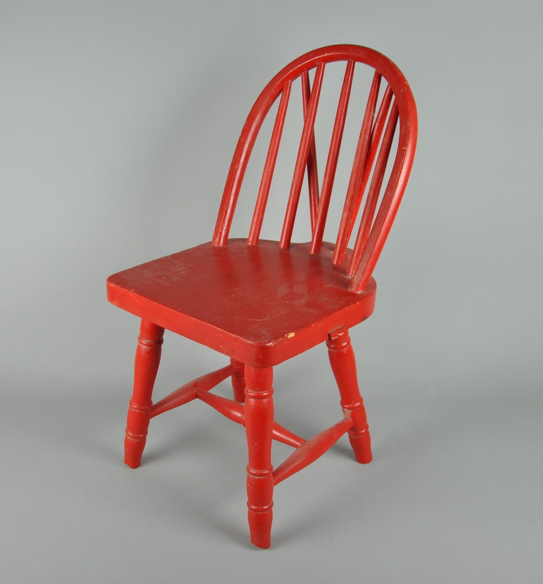 Rødmalt barnestol av tre. Stolen er formet som en budalsstol.