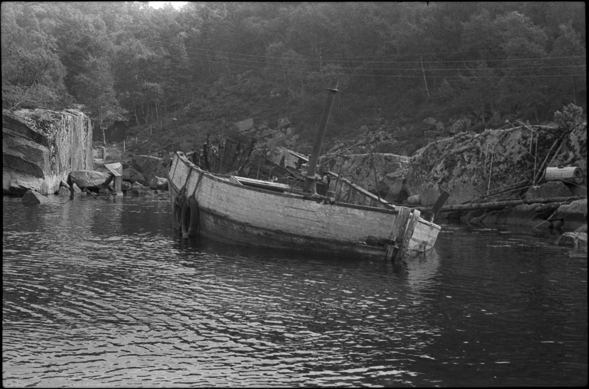 Vraket av fiskebåten M/S "Familien" ligger ved strandsonen i ei vik i Ålfjorden, Hordaland. Det er to hytter og et naust i nærheten.