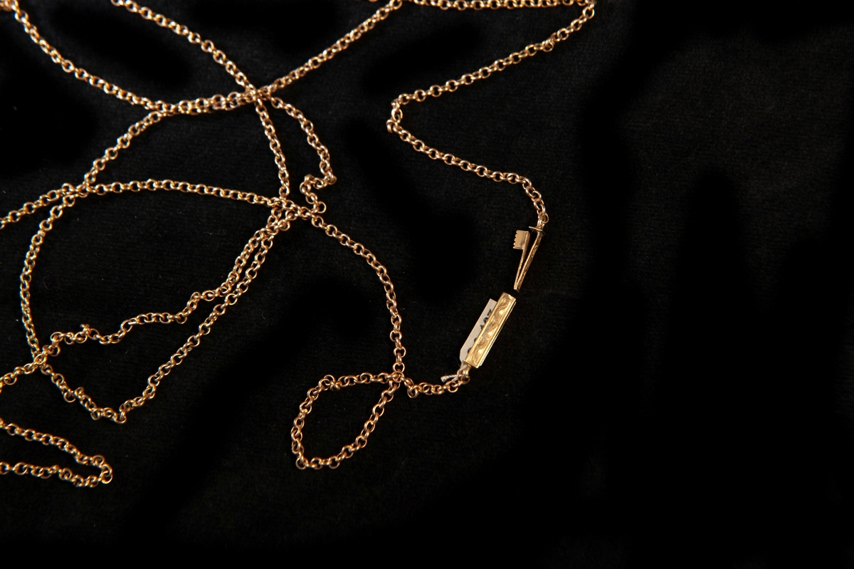 Lång halskedja av guld (enkel modell). Sticklås med graverad dekor av slingor.