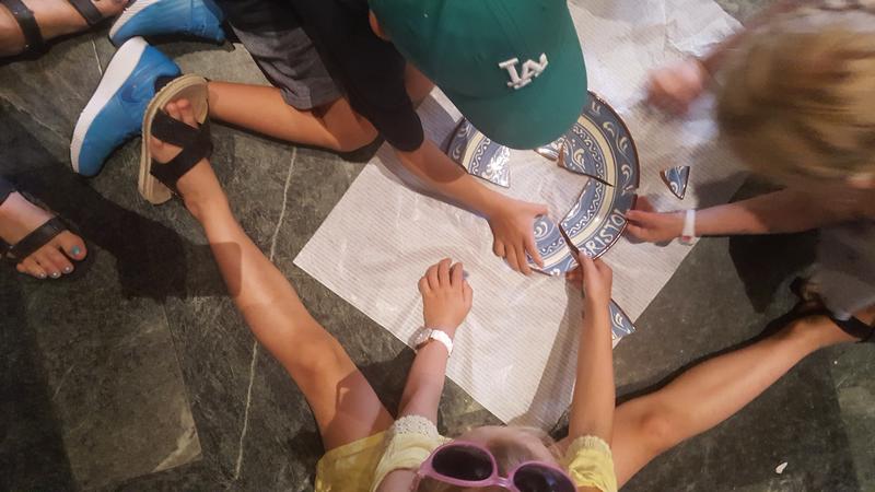 Barn som sitter på et gulv og setter sammen en knust keramikk tallerken