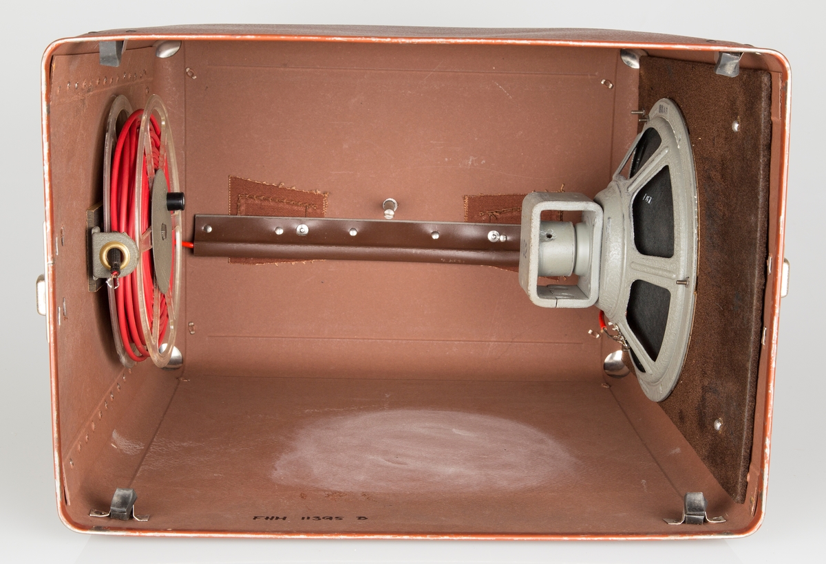 Filmfremviser i brun transportkoffert. For 8mm smalfilm. Kofferten fungerer som fundament for fremviseren. Høyttaler i  lokket. Koffertbunnen har 5 gummierte føtter.