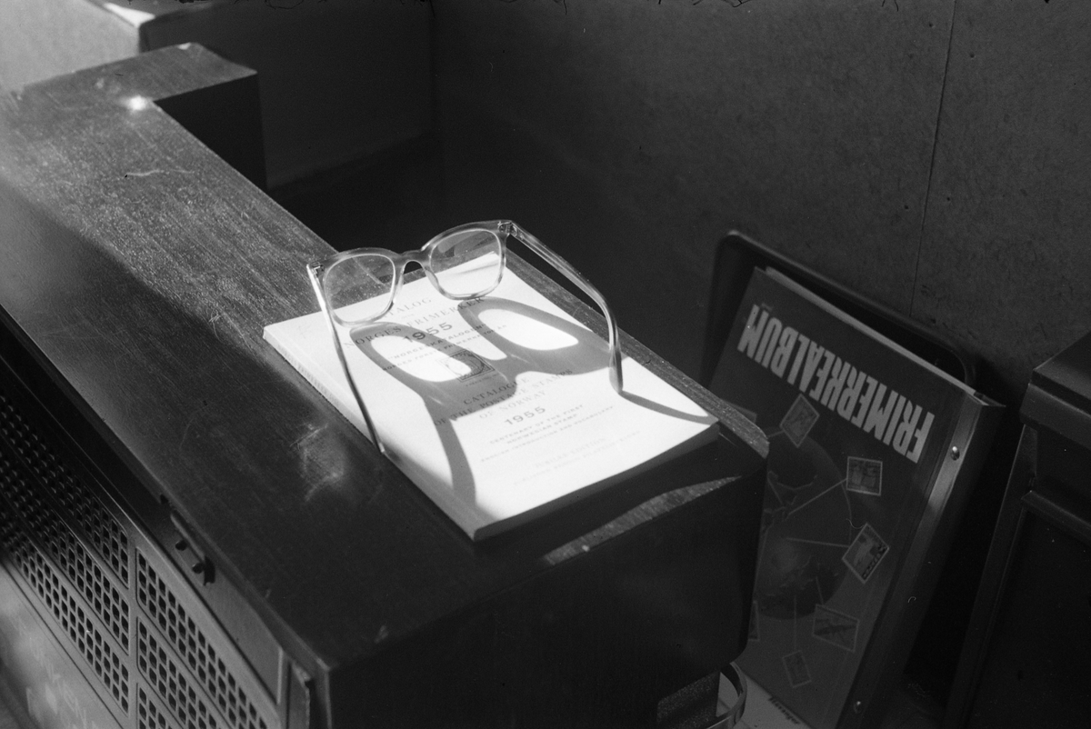 Ei bok og et par briller ligger på toppen av et radioapparat. Sidelys kaster skygge fra brillene.