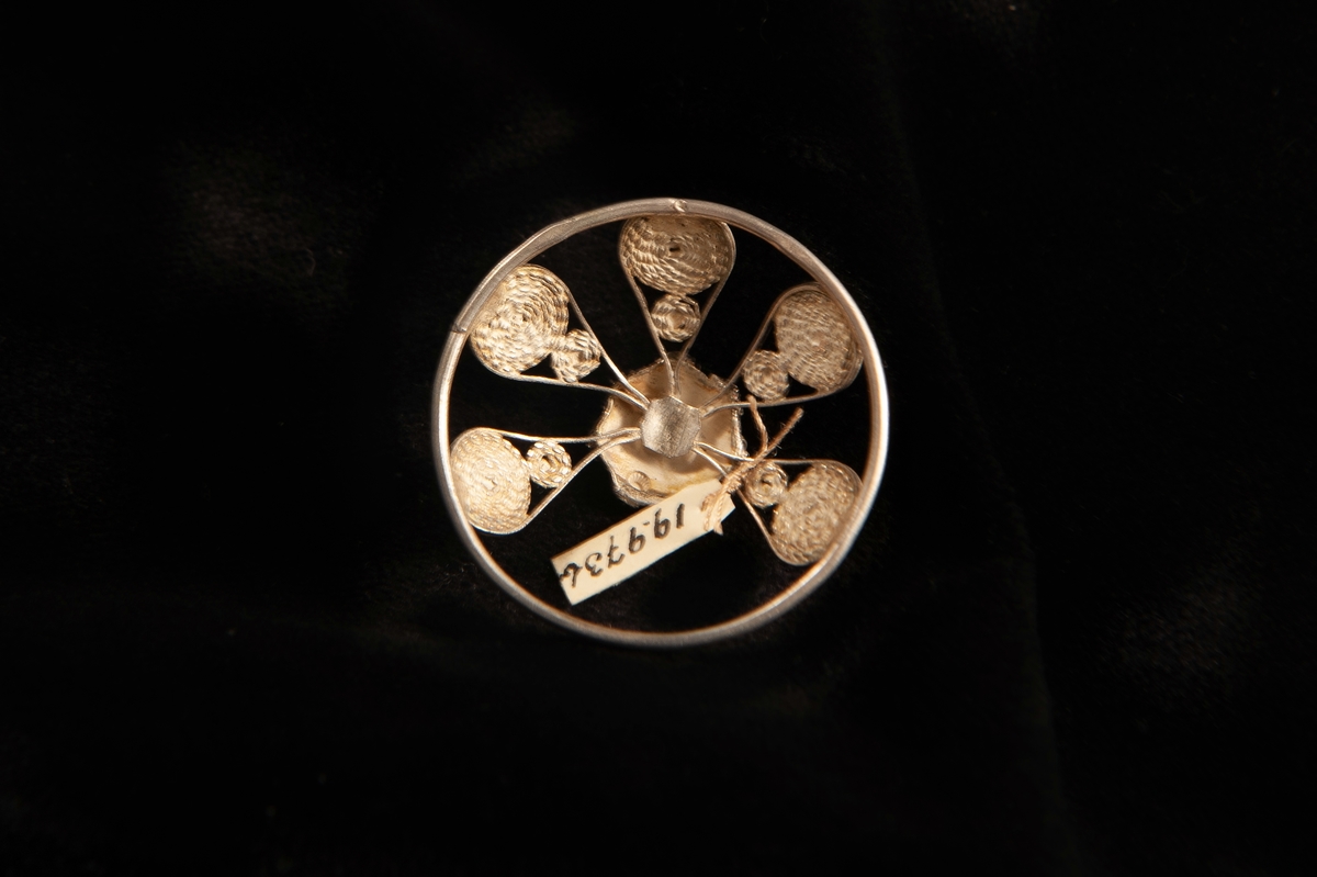 En malja av silver. Filigranarbete i form av fem "tungor" upp mot blomma i filigran. Stämplad på rundelns kant. JM.19973:a-e hör ihop.
