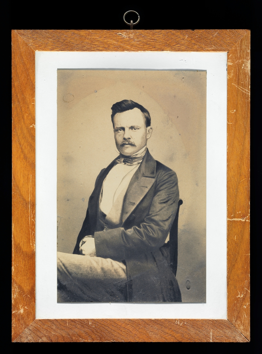 Fotografisk portrett av den tyske forstmannen Friederich Casimir Gustav Heyer (1826-1883), vanligvis bare omtalt som Gustav Heyer. Han er avbildet sittende på en stol i et fotografisk studio.  Heyer var kledd i ei lang, frakkeliknende jakke med store slag, med vest og kvit skjorte under.  Om hanlsen har han knyttet et silketørkle.  Da detet fotografiet ble tatt var den kjente forstmannen antakelig i 30-40-åra.  Han hadde bart og skrått bakoverstrøket, mørkt hår.  Gustav var sønn av Karl Heyer, som var professor ved det kjente skogakademiet i Giessen i den tyske delstaten Hessen.  Gustav gikk på gymnas hjembyen, og etter at han hadde tatt artium satt han åtte semestre under (1843-1847) under farens kateter.  Deretter reiste han ut og praktiserte et par år, før han vendte tilbake til Giessen i 1849-1850.  Der var han først «privatdosent» en periode, inntil han i 1853 ble utnevnt til professor med forvaltningsansvar for skogene i området.  Med de erfaringene dette gav ham fikk han også undervisninsplikt i praktisk skogbehandling.  Gustav Heyer gjorde seg bemerket som en dyktig fagmann, og han skal ha blitt tilbudt professorater både i Zürich og Karlsruhe, tilbud han avslo, angivelig fordi han var så sterkt knyttet til hjemtraktene.  I 1868 sa han derimot ja til et tilbud om å bli direktør for det prøysiske forstakademiet i Münden, et embete som gav høyere lønn, samtidig som Heyer visste at det forstinstituttet i Giessen var truet av omorganiseringer.  I 1875 skal han ha søkt et professorat ved den østerrikske «Hochschule für Bodenkultur», en stilling Heyer ikke fikk.  Etter dette skal han ha bestemt seg for å bli i Tyskland.  Som skogakademiker skal Gustav Heyer ha gjort seg bemerket med uvanlig bred naturfaglig innsikt, og som en klartenkt fagmann som visste å formidle sin faglige kompetanse så vel muntlig som skriftlig. Hans egen forskning var først og fremst knyttet til det skogøkonomiske fagfeltet, men han underviste og skrev også med suksess i mer produksjonsrelaterte emner som skogkultur og skognytting. 