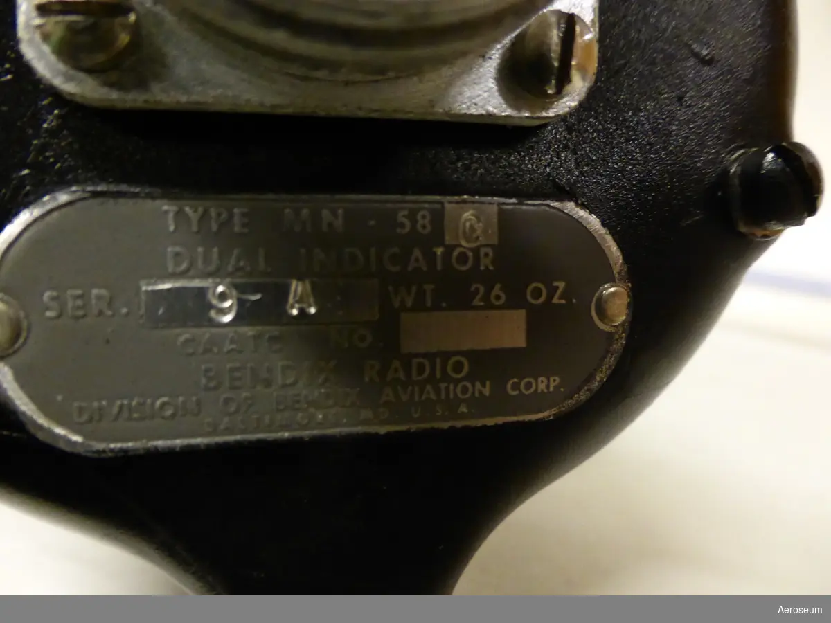 En svart radiokompass för flygplan.

Innanför glaset där siffror och visare finns står det i mitten: "RADIO COMPASS BENDIX RADIO".

På baksidan av föremålet står det: "TYPE MN. 58C", "DUAL INDICATOR", "SER. 9 A WT. 26 OZ.", "CAATC NO.", "BENDIX RADIO", "DIVISION OF BENDIX AVIATION CORP.", "BALTIMORE. MD. U.S.A.".