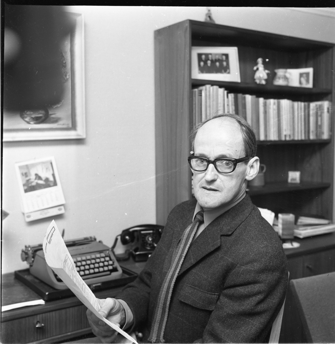 Fingalsson sitter vid ett bord med en skrivmaskin intill sig, håller ett papper i handen.