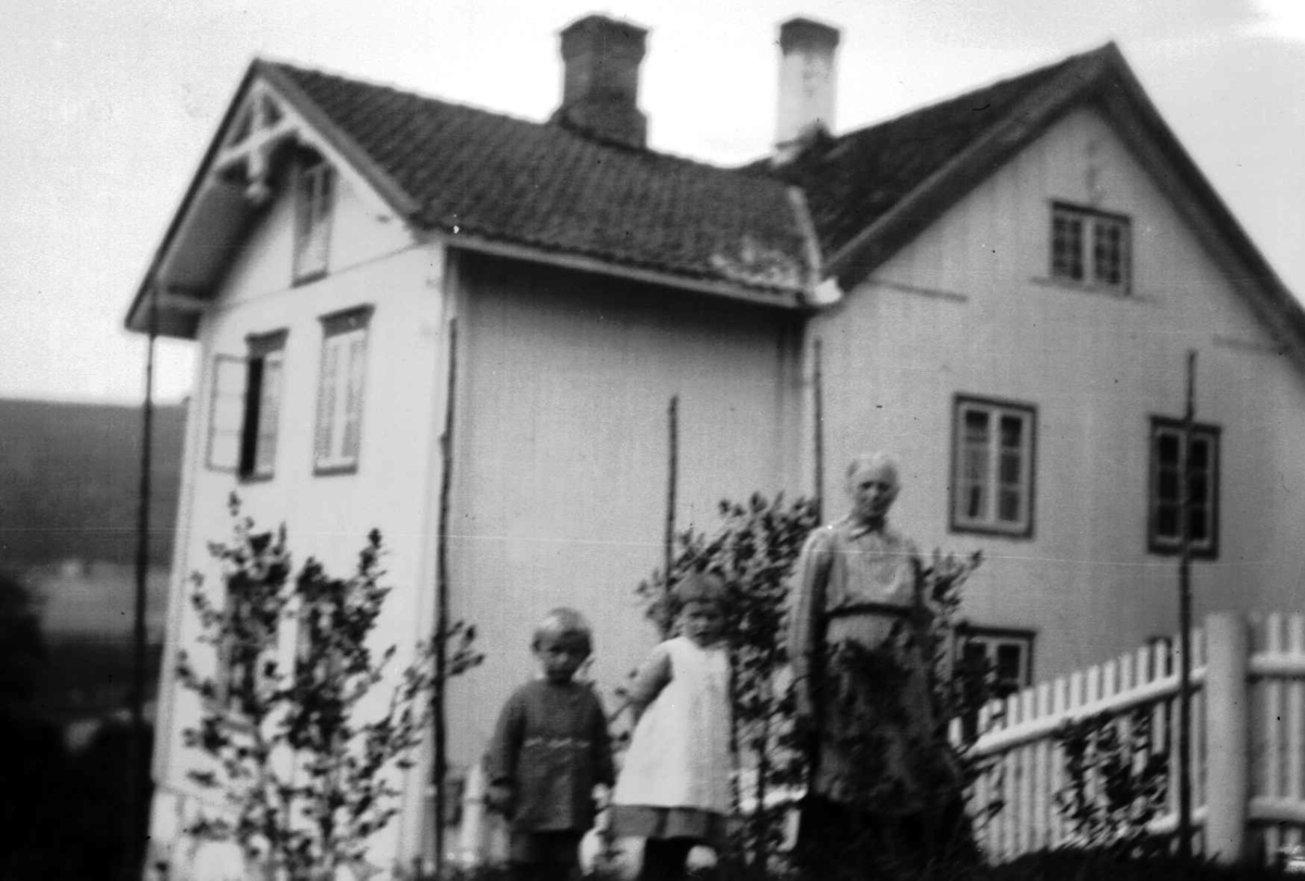 Agnethe Jørstad utenfor utenfor et hus, antagelig vis med to av barnebarna