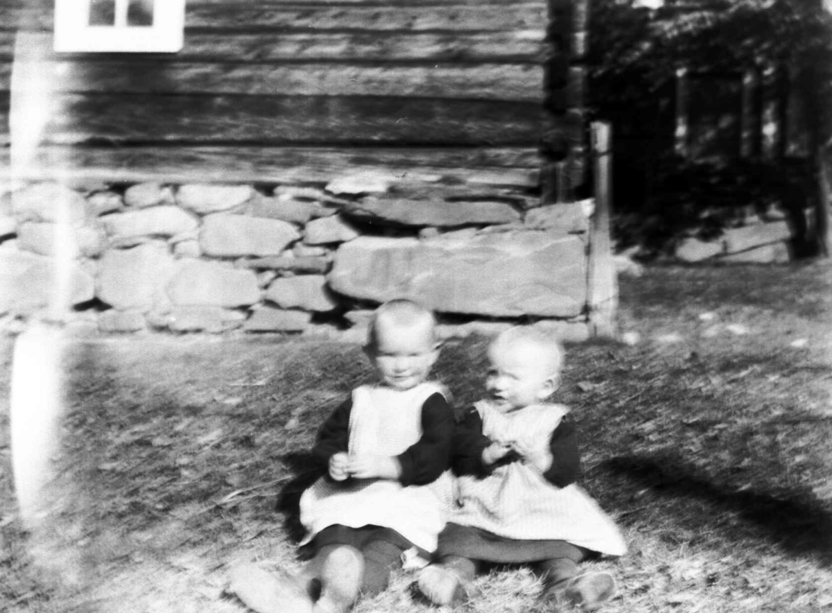 To småbarn utenfor en tømmerbygning.
