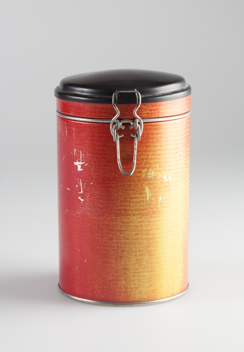 Sylinderformet boks med hengslet lokk som festes med patentlås.