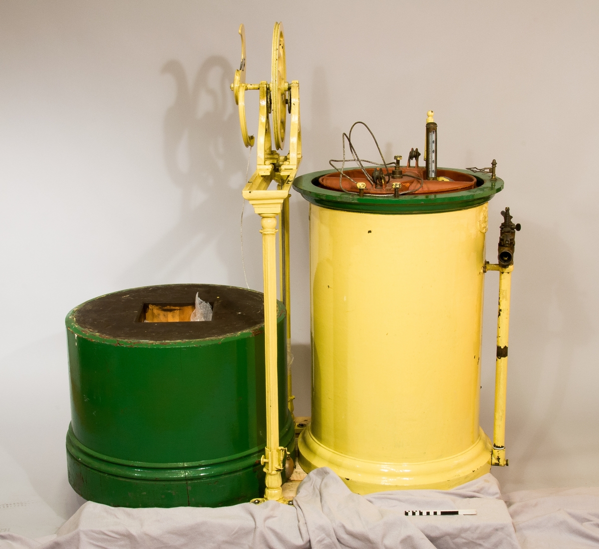 Gasklocka målad i gul och grön färg. Har texten "The gas meter Co, limited makers Oldhall works" på sig.
