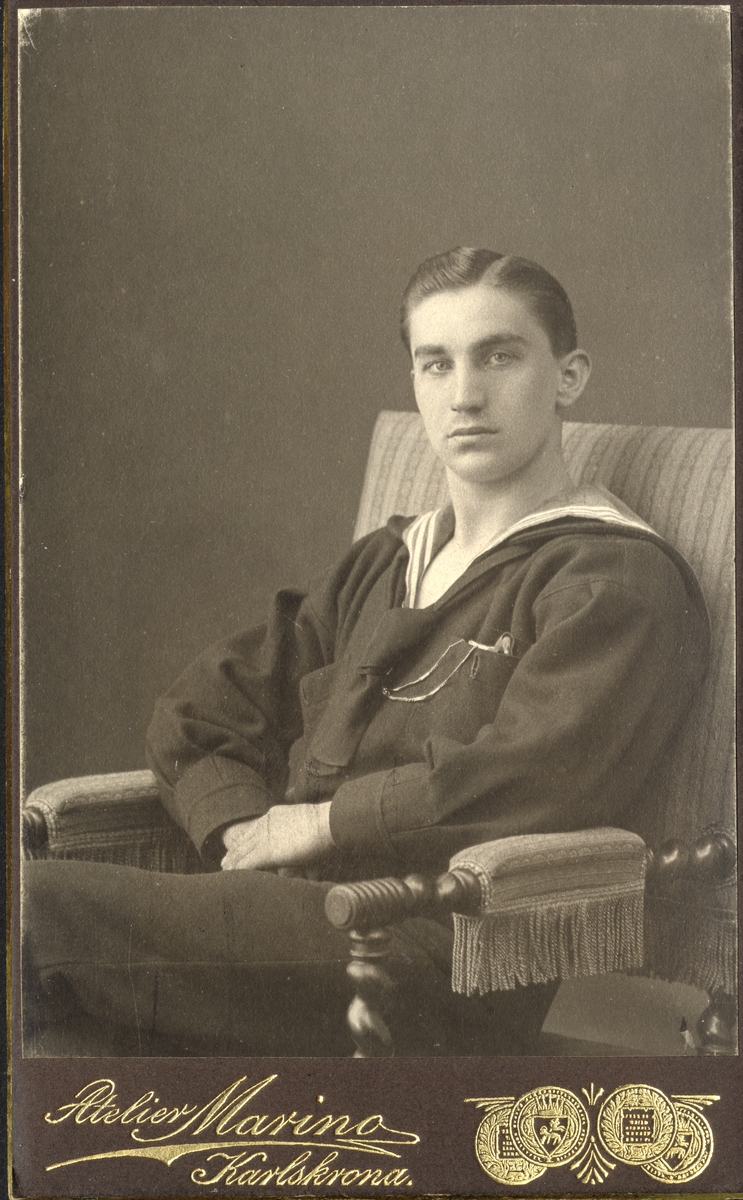 Porträttfoto av en sittande okänd man i flottans uniform. 
Knäbild, ateljéfoto.