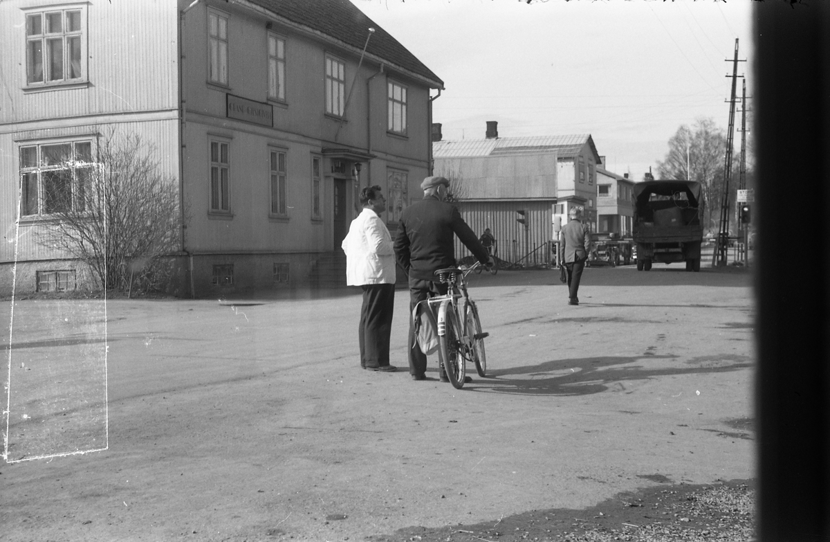 Gatebilde fra Lena 1958. Mannen med sykkelen er ikke identifisert, men han til venstsre er Arild Brandt-Johannessen. Bildet er tatt gjennom vinduet i Lena Foto & Radio i "Raubua".