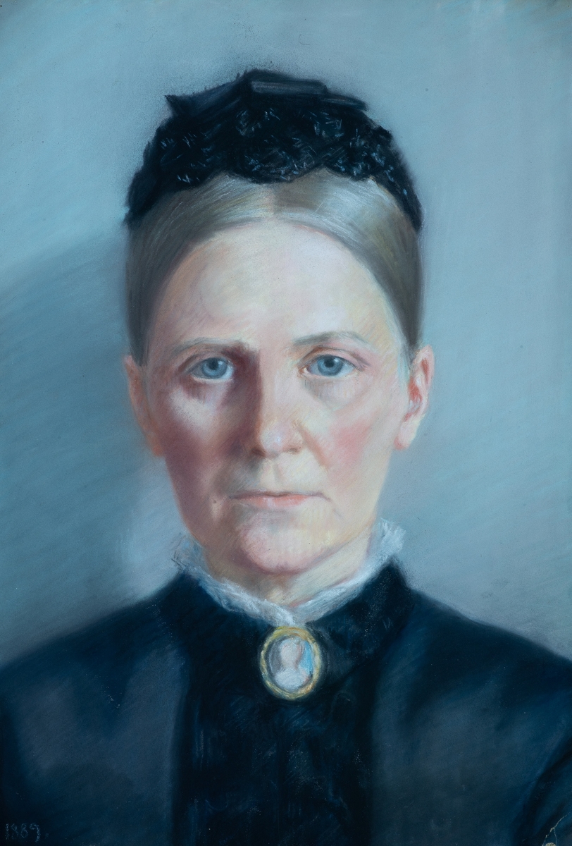 Portrett av Marie Blom,  f. Mangor (1837-1917),  1889.  Kvinneportrett en face,  lyst grått hår med midtskill, sort kappe.  Avskåret over skuldrene.   Sort kjole, smal hvit rysj i halslinningen. Hun har på seg brosje med miniatyr  AAMB 1174, antagelig av hennes mors farmor Sara Juell  f. Chrystie. Grå øyne, rødlig karnasjon, lys grå  bakgrunn.