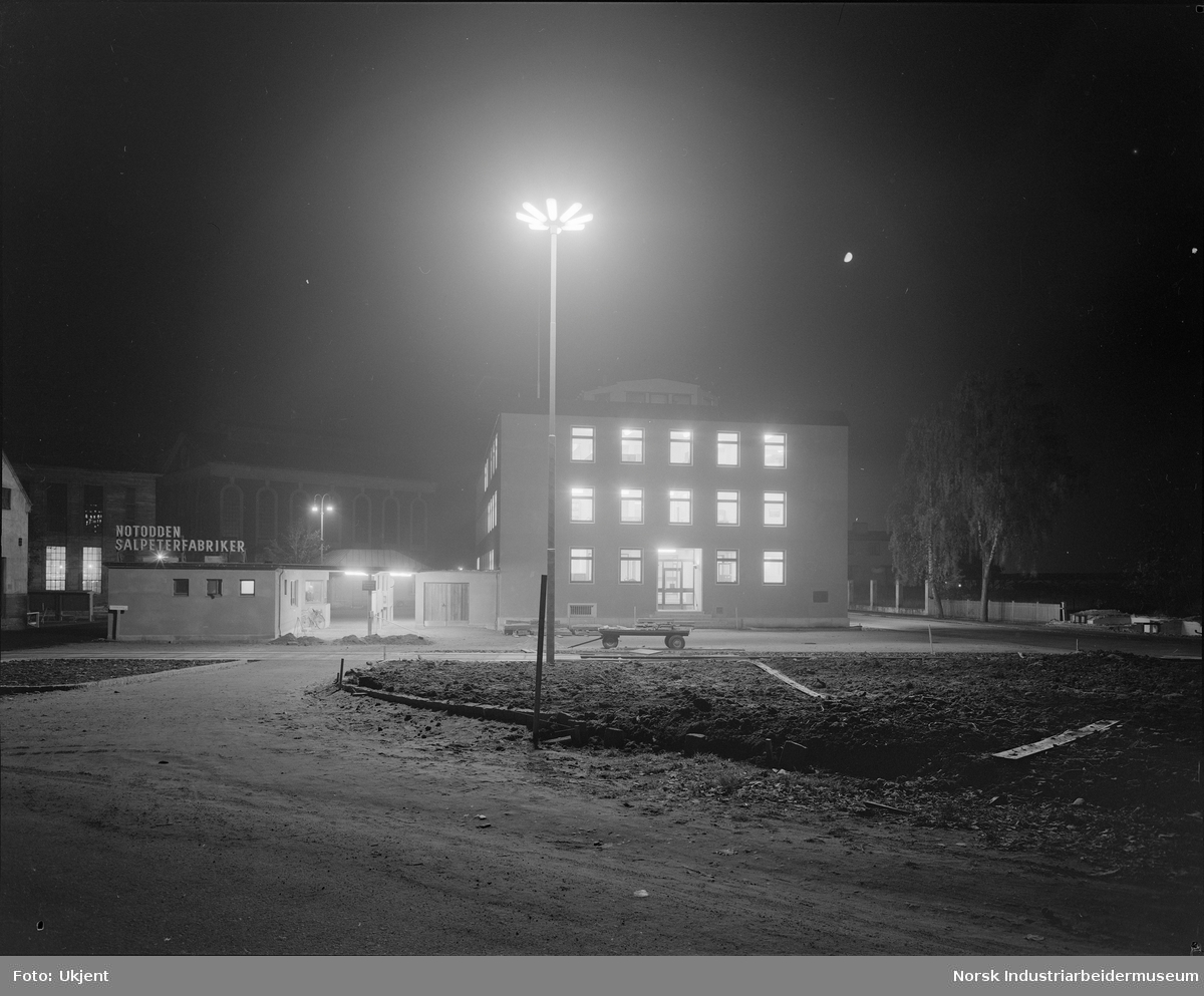 Kveldsbilde. Kontorbygget i Hydroparken (bygg 1, oppført 1955).
Portvakta med inngang til fabrikken (midt i bildet) og Notoddens første jernbanestasjon t.v.