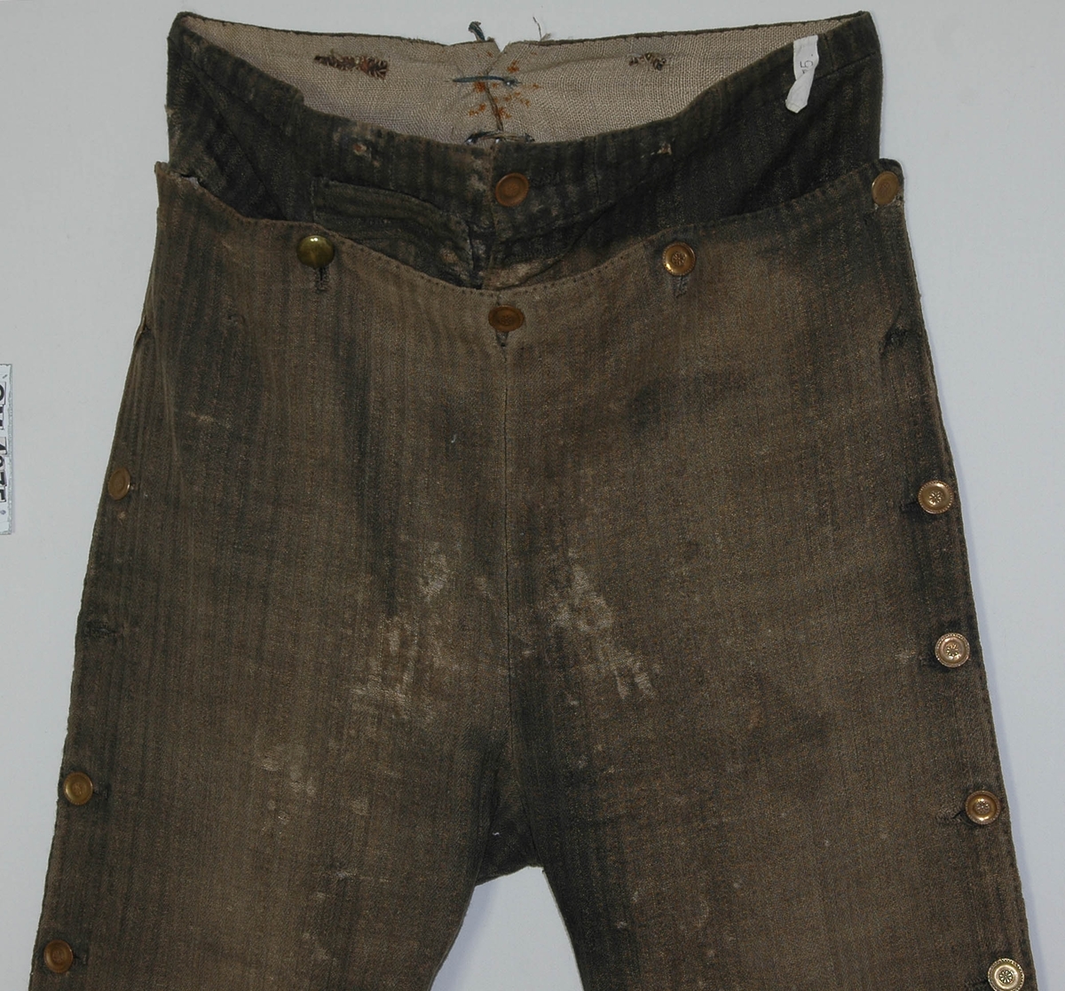 Uniformsbyxa från 1800-talet början.
Byxorna är grårandiga med knäppning i sidan med platta bronsknappar, med särskild linning av samma tyg upptill på framsidan.