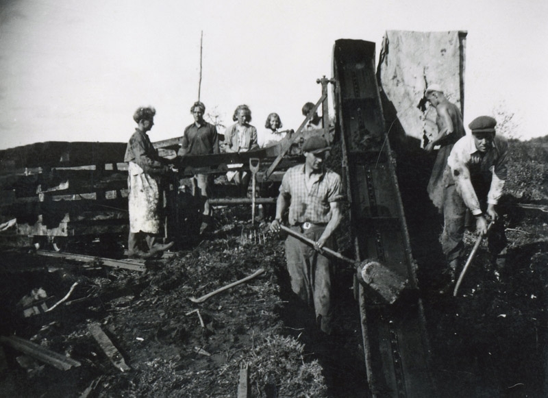 Män arbetar med torvupptagning vid Götaverkens mosse i Tulebo, 1940-tal. Några personer står bakom ett staket och tittar på.