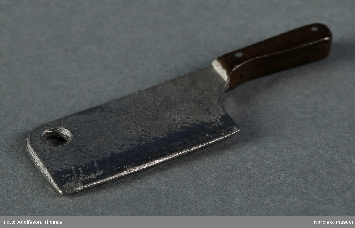 Köttkniv av metall med trähandtag. Hör till köksinredningen på första våningen i dockskåp NM.0331721+.