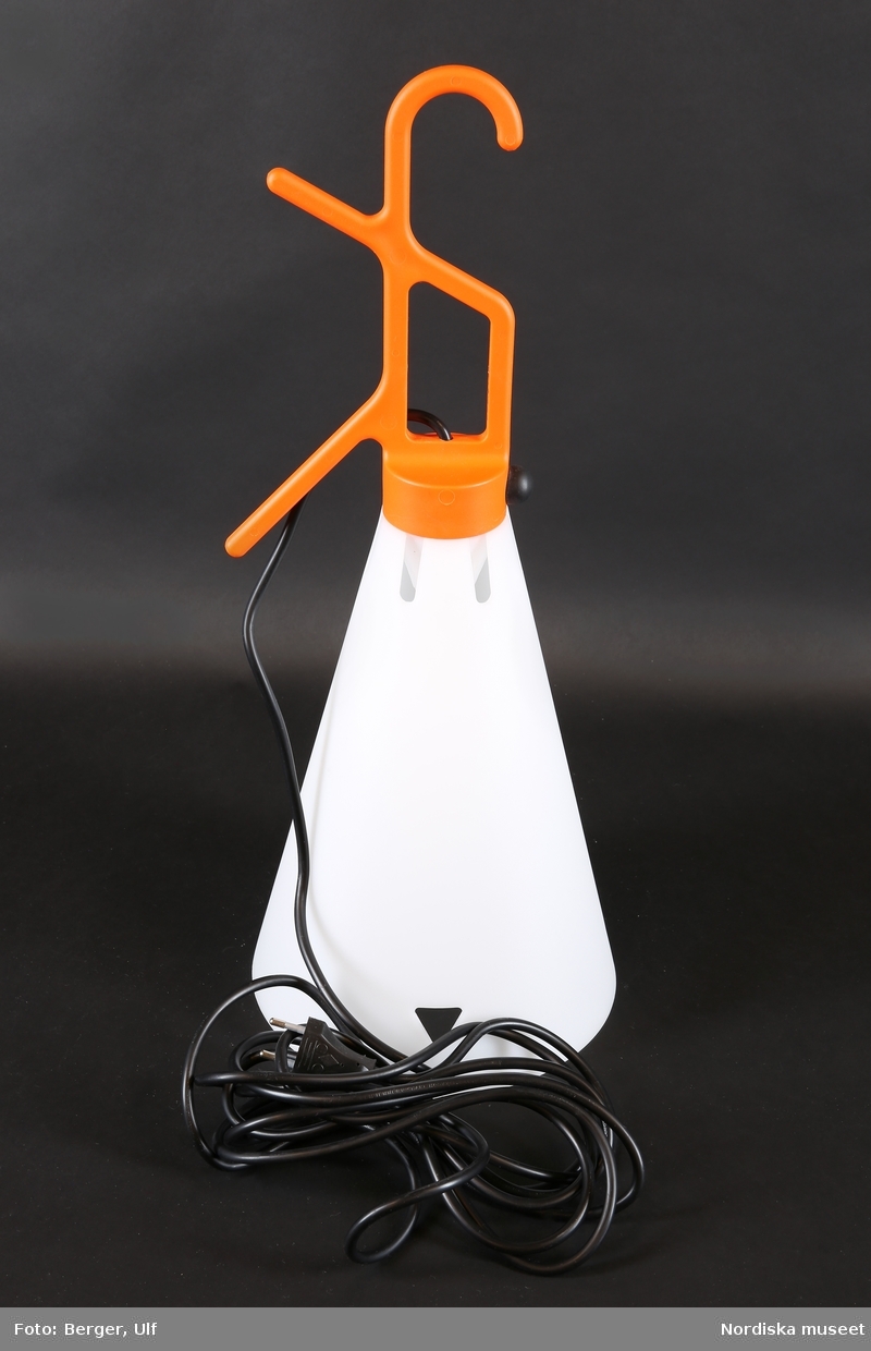 a-b)
a) Konisk lampskärm av vit plast upptill avslutad i upphäng med krok och två piggar i orange färg. b) LED-lampa inuti skärmen. Svart rund knapp på upphänget utgör strömbrytare. Kroken gör det möjligt att enkelt flytta lampan och hänga upp den var som helst. Lampan kan också ställas på skärmen. De två piggarna används till att rulla upp sladden på.
/Maria Maxén 2018-04-11.