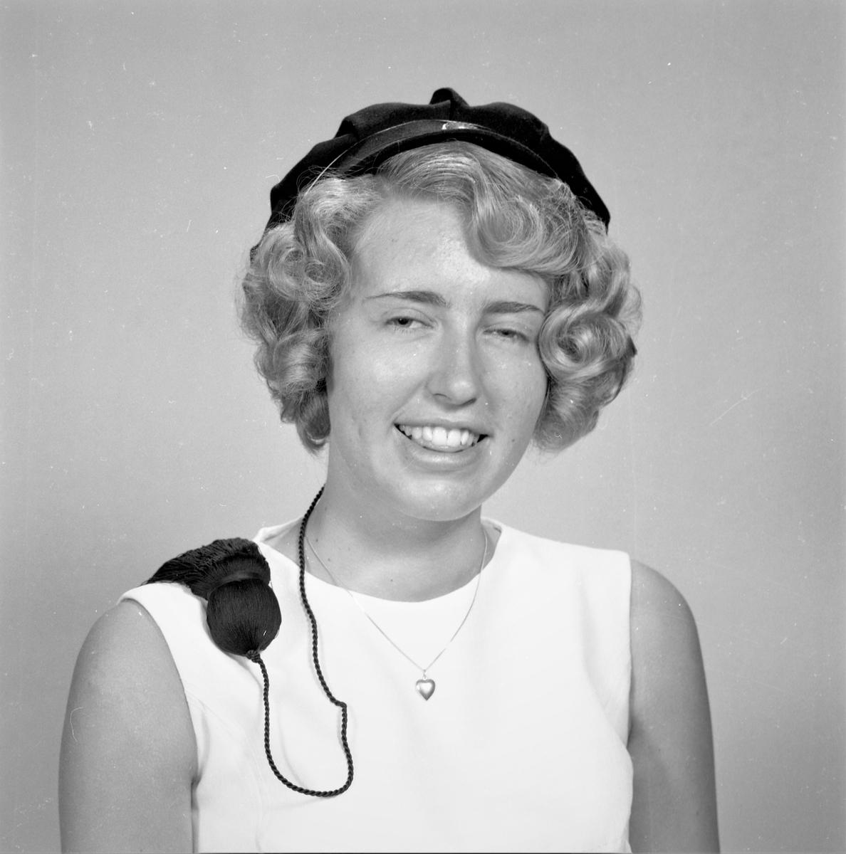 Portrett. Ung lyshåret kvinne i lys ermeløs kjole. Sort studentlue på hodet. Bestilt av Vigdis Hvalberg. St. Olavsgt. 13c