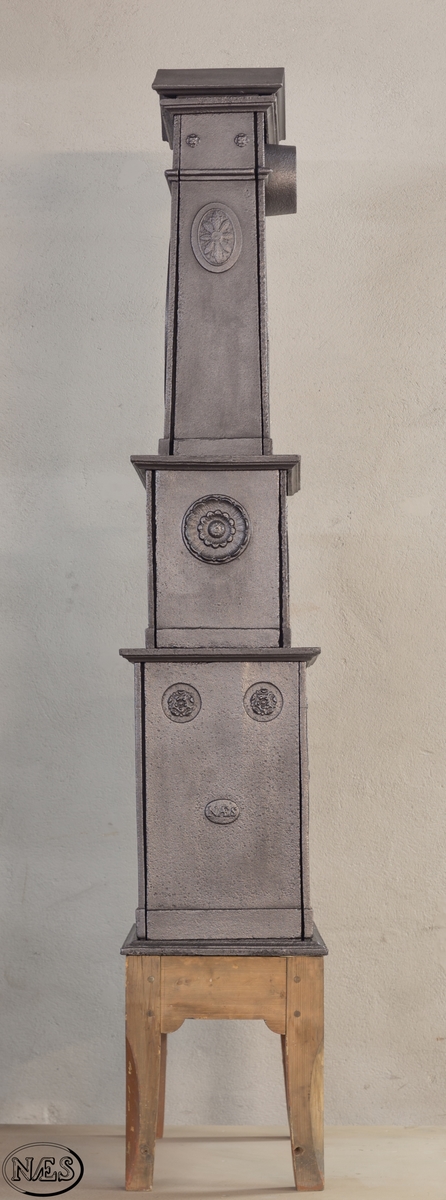 Ovn i to etasjer med obeliskform på toppen. Avsluttes med en gavl. På ovnens langside 1.etg - Frukt og blomstervase i liggende oval. Ovnsdør på kortside og innskrift på motsatt kortside. Langside 2.etg har en rundbuet åpning med en rosett i hvert øvre hjørne. Stor rosett på kortside. Obeliskformen har et stående ovalt gittervindu på langsiden. Ventiler i 2. og 3. etg.