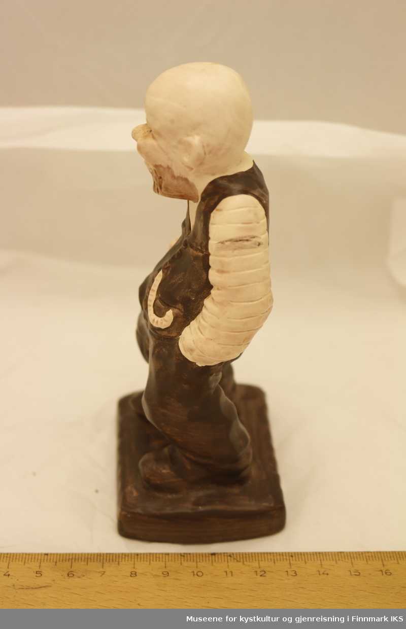 En malt porselensfigurin av en mann med skjegg, ikledd 1800-talls klær med vest og skjorte og lommeur. 